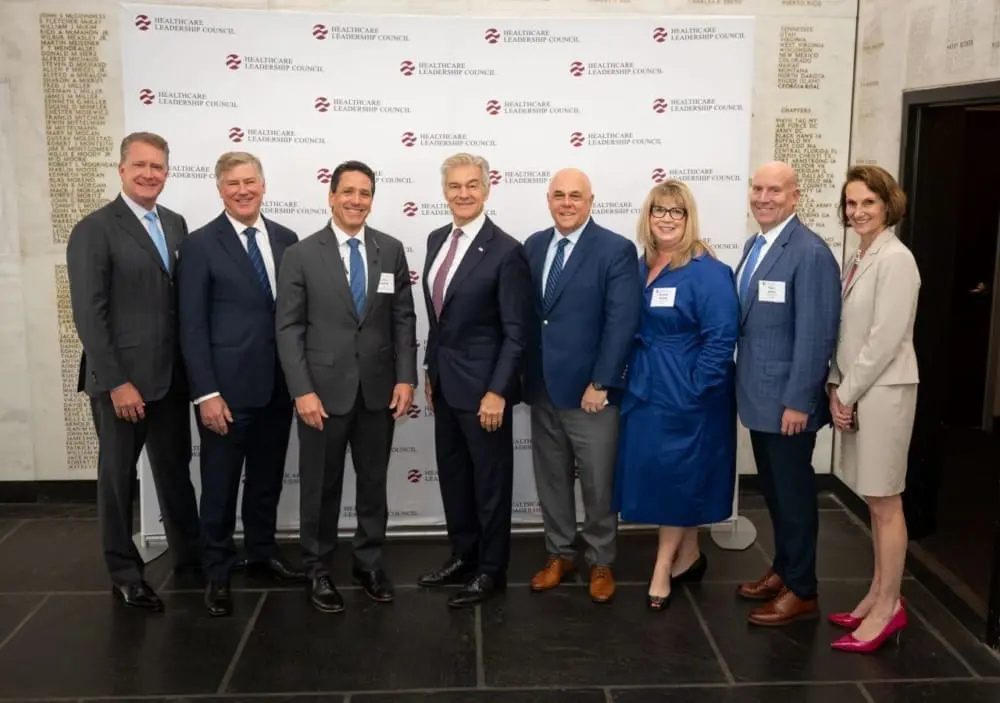 A group of six men and two women stand side by side in business attire and smile for the camera.