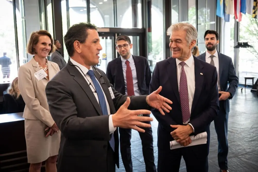 A group of individuals in business attire stand in a lobby and chat.