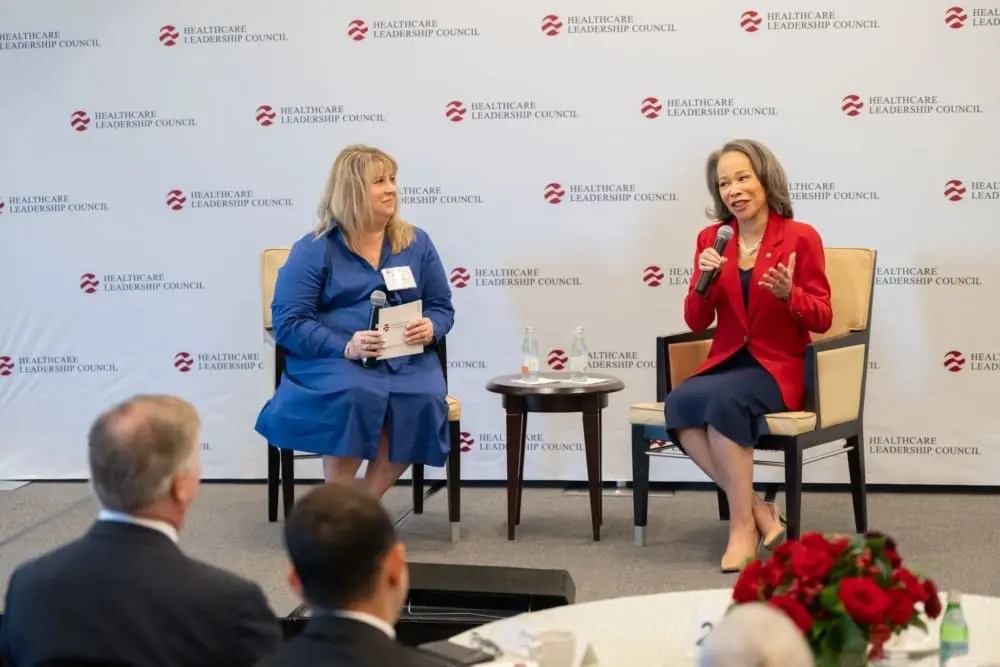Two women sit on a stage in front of a Healthcare Leadership Council banner. They both hold microphones.