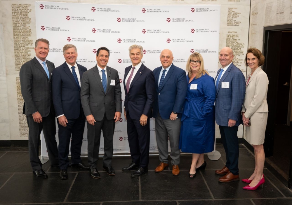 A group of six men and two women stand side by side in business attire and smile for the camera.