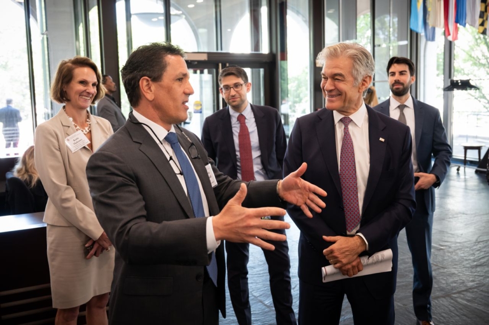 A group of individuals in business attire stand in a lobby and chat.