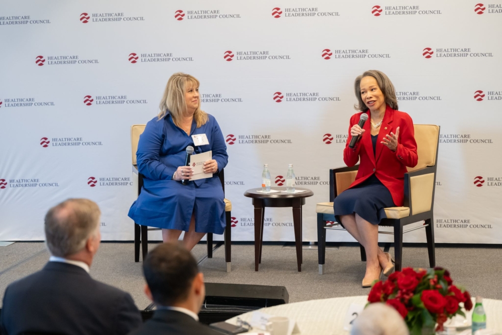 Two women sit on a stage in front of a Healthcare Leadership Council banner. They both hold microphones.