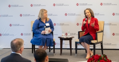 Two women sit on a stage in front of a Healthcare Leadership Council banner. They both hold microphones.