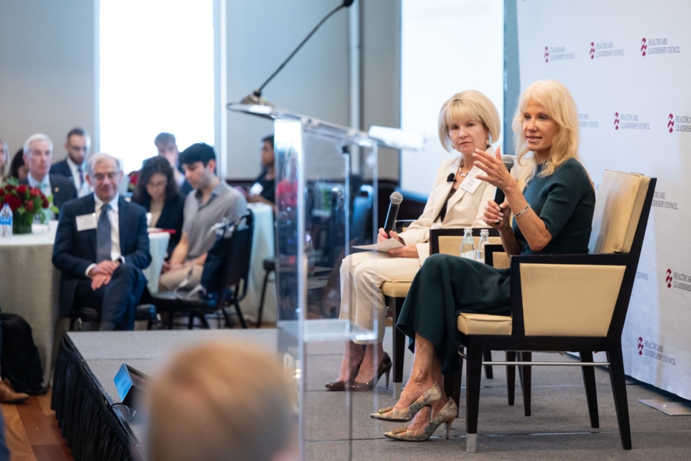 Two women sit on a stage in front of a Healthcare Leadership Council banner. They both hold microphones.